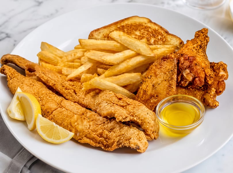 Fried fish and chicken wings with french fries, toast, lemon wedges, and dipping sauce.